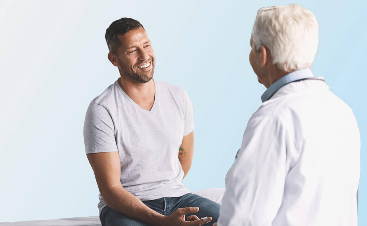 Man on examination table being talked to by a doctor.