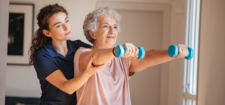 Physical therapist helping elderly woman lift weights to build muscle