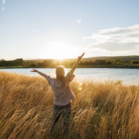 Carefree woman with arms raised feeling connection and harmony with nature elaxed woman enjoying fresh air at windy lake during autumn sunset. Freedom and happiness outdoors
